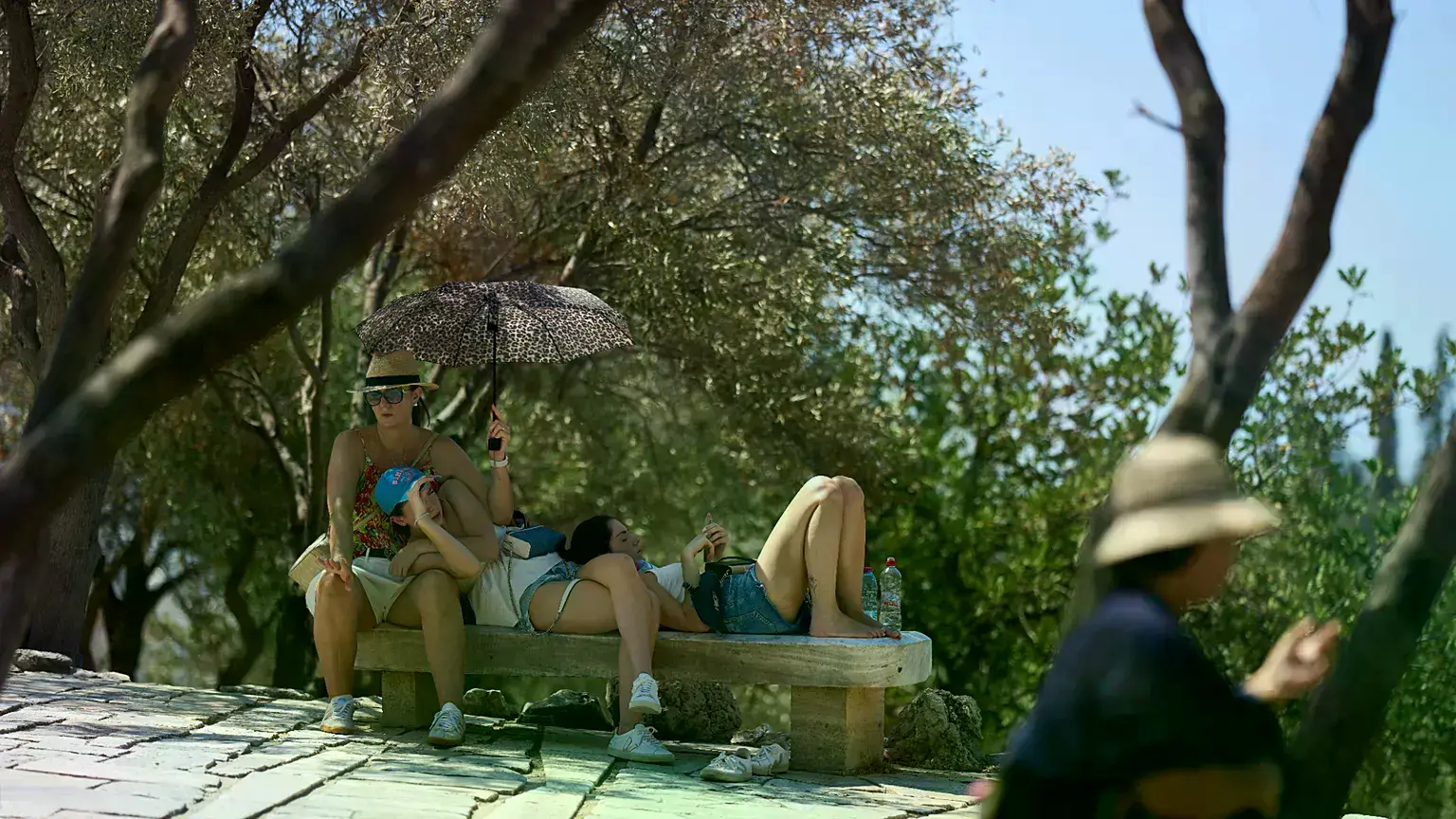 Turistas descansan bajo un paraguas frente a la Acrópolis durante una ola de calor en Atenas, julio de 2025.
