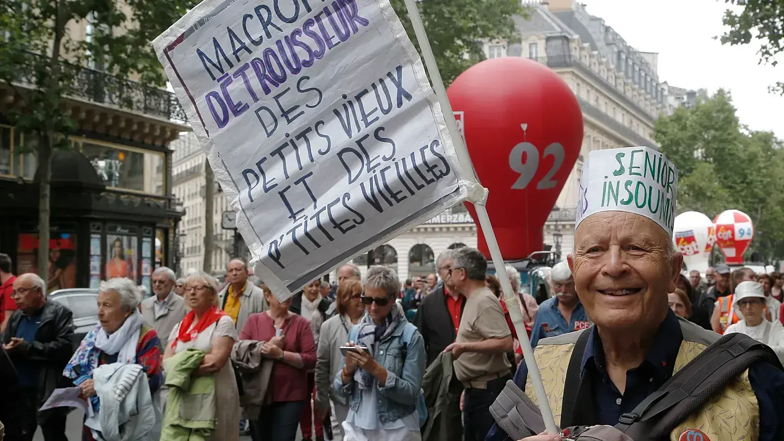 Un jubilado sostiene una pancarta en la que se lee 'Macron roba el dinero a viejitos y viejitas' durante una manifestación en
