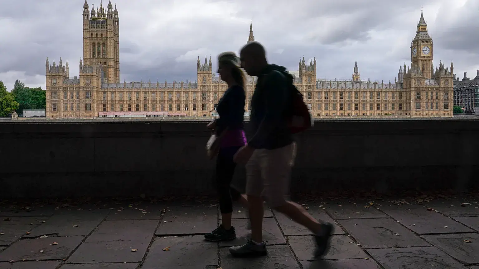 Personas caminan por la margen sur del río Támesis, con el Palacio de Westminster al fondo, en Londres.