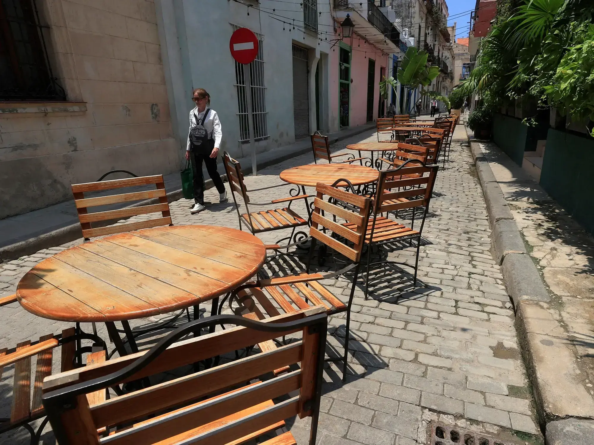 Una persona camina frente a mesas y sillas vacías en La Habana, símbolo de la crisis turística.