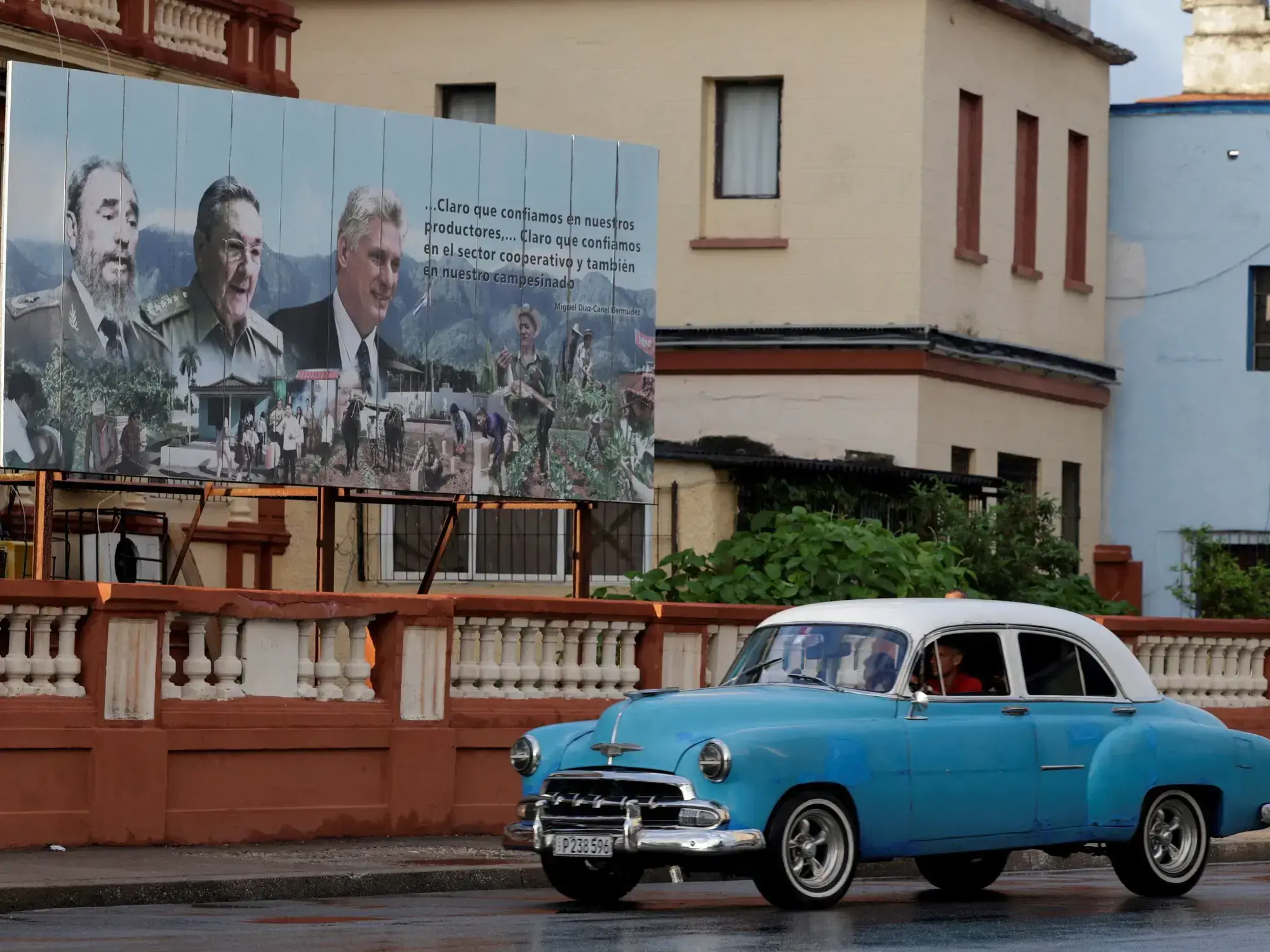 Un auto pasa junto a una imagen de los hermanos Castro y Miguel Díaz-Canel.