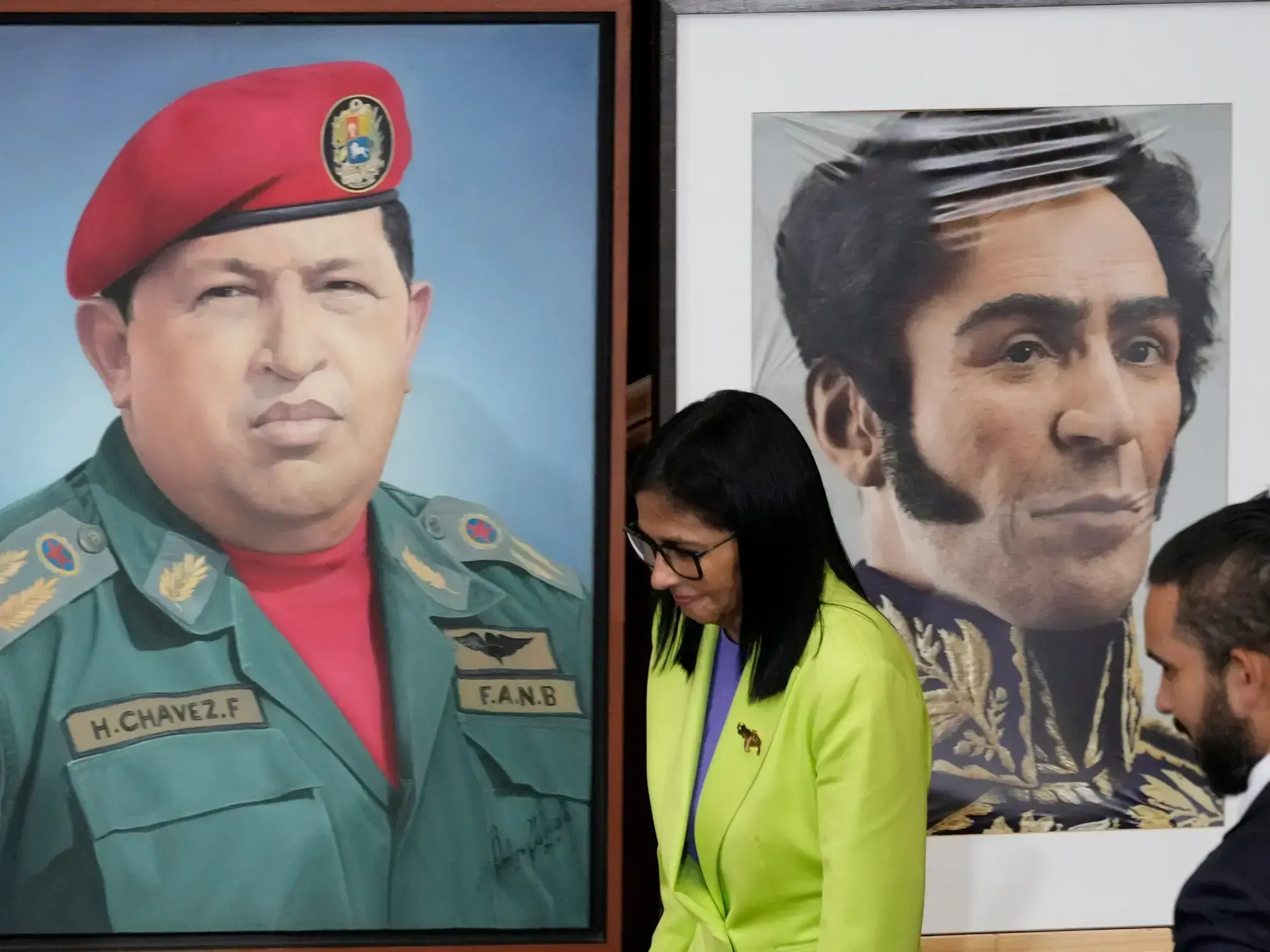 La presidenta interina de Venezuela, Delcy Rodríguez, pasa junto a una imagen del expresidente Hugo Chávez (izquierda) y del