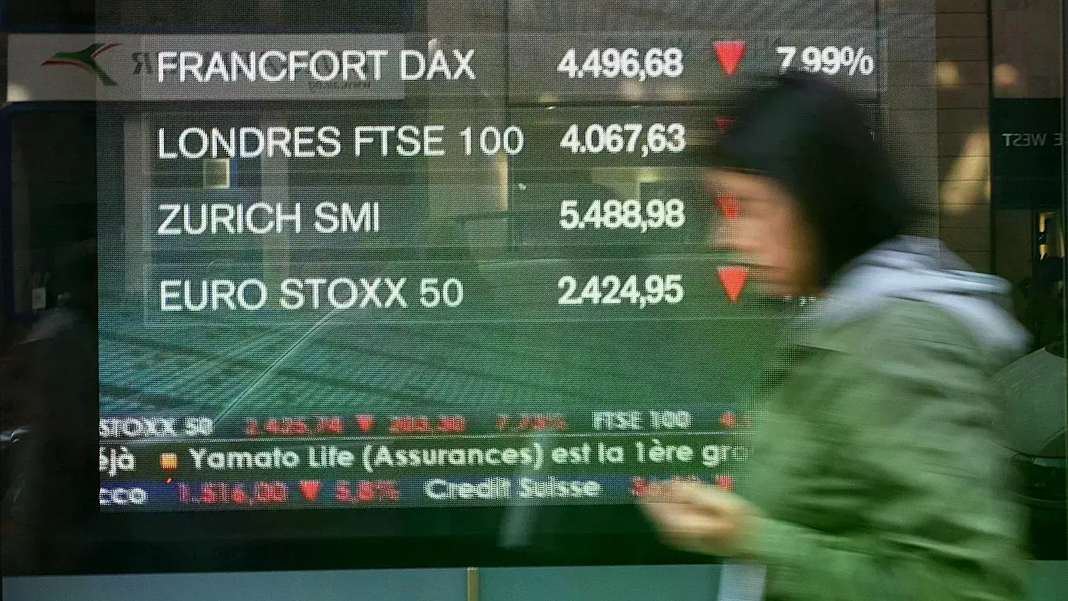 Un peatón pasa junto a una pantalla que muestra noticias de los mercados con los índices de las bolsas europeas, el viernes d