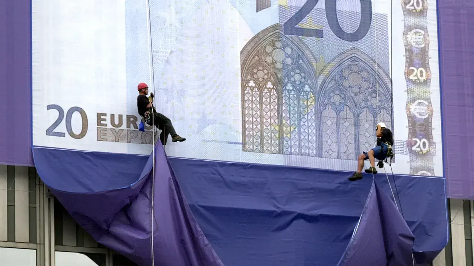 Montañeros descienden en rápel desde la sede del Banco Central Europeo para desplegar réplicas gigantes de los nuevos billetes de euro durante la presentación de la moneda.