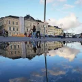 Personas caminan por una plaza reflejada en un charco en Helsinki, Finlandia.