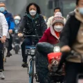 Personas con mascarillas circulan en bicicleta por el distrito financiero de Pekín.