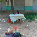 Niña haciendo tarea escolar en una mesa junto a recipientes con gasolina.