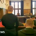 Los acusados comparecen en un tribunal de Varsovia con uniforme naranja y esposas.