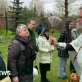 Personas hacen cola para ser rociadas con agua bendita por un sacerdote en Kharkiv.
