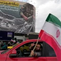 Un hombre celebra con una bandera de Irán bajo un cartel que ridiculiza a las fuerzas de Estados Unidos en Teherán.