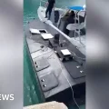 Momento en que el dron naval descubierto (izquierda) es remolcado por un guardacostas griego al puerto de Vasiliki.