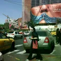 Transeúntes y autos en una esquina de Teherán, con Trump de fondo.