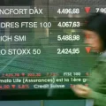 Un peatón pasa junto a una pantalla que muestra noticias de los mercados con los índices de las bolsas europeas, el viernes d